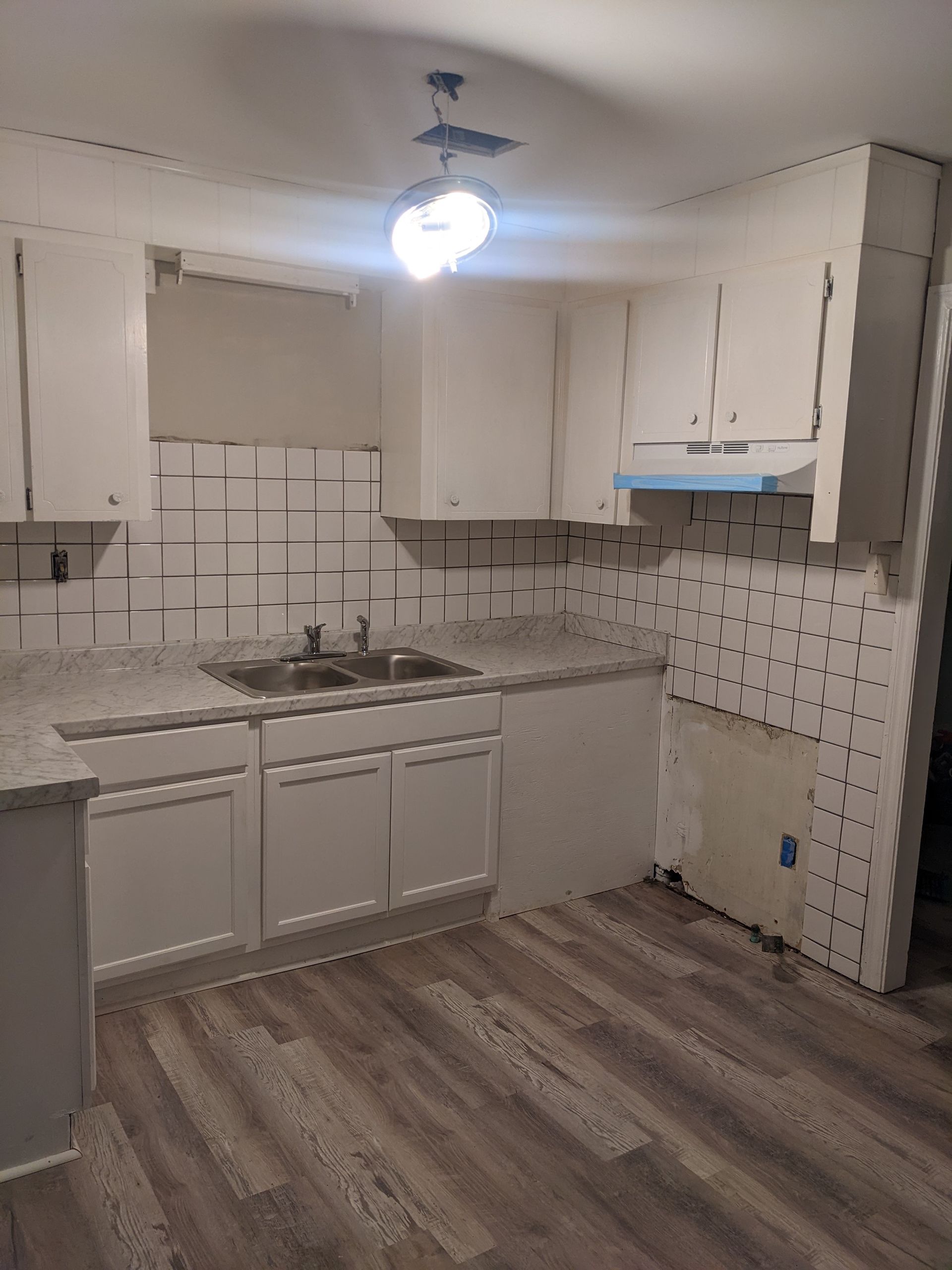 An empty kitchen with white cabinets and a sink.
