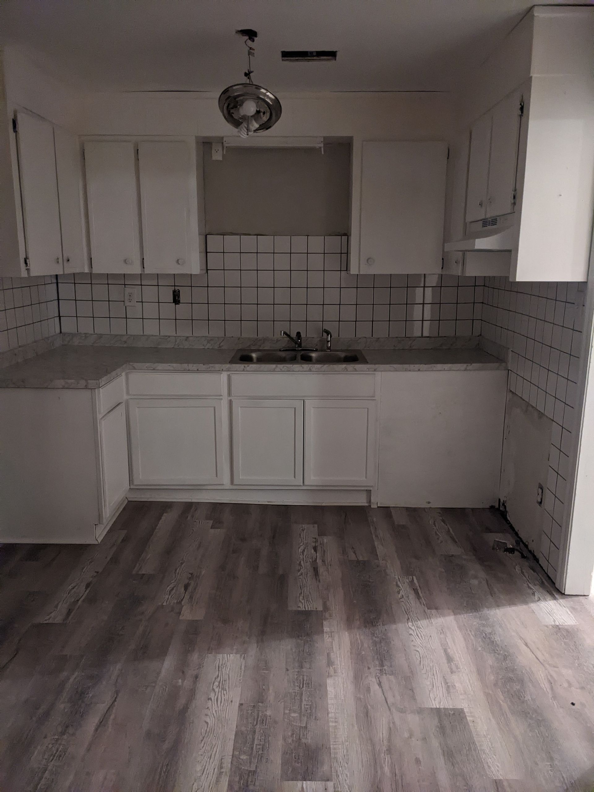 An empty kitchen with white cabinets and a sink.