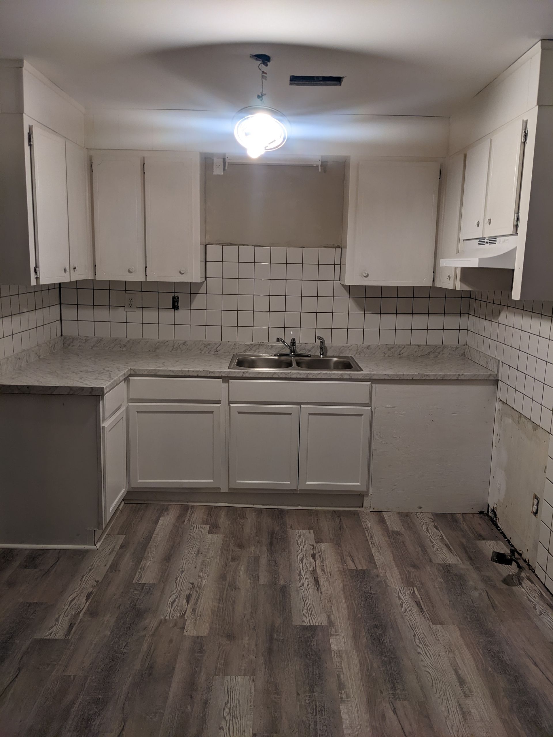 An empty kitchen with white cabinets and a sink.