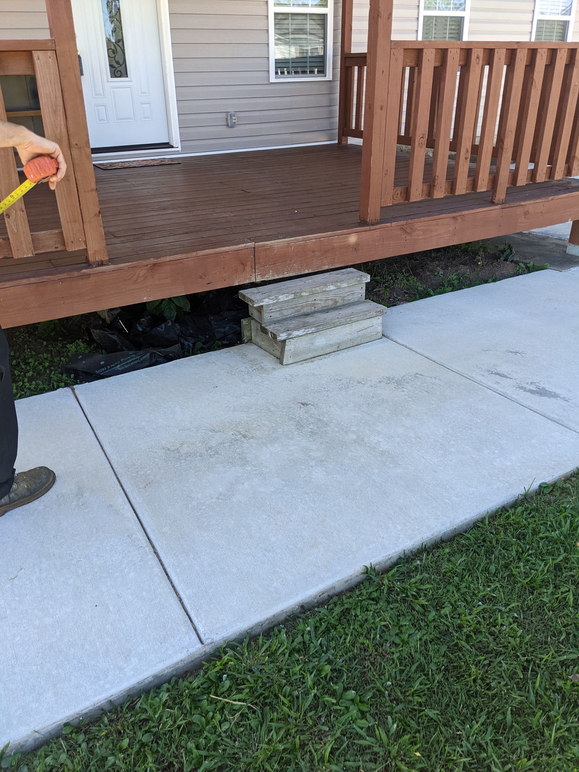 A person is measuring a concrete walkway next to a wooden deck.