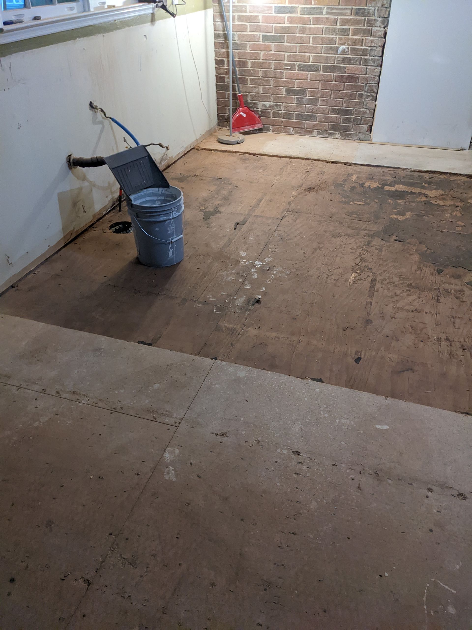 A bucket is sitting on the floor in a room with a brick wall.