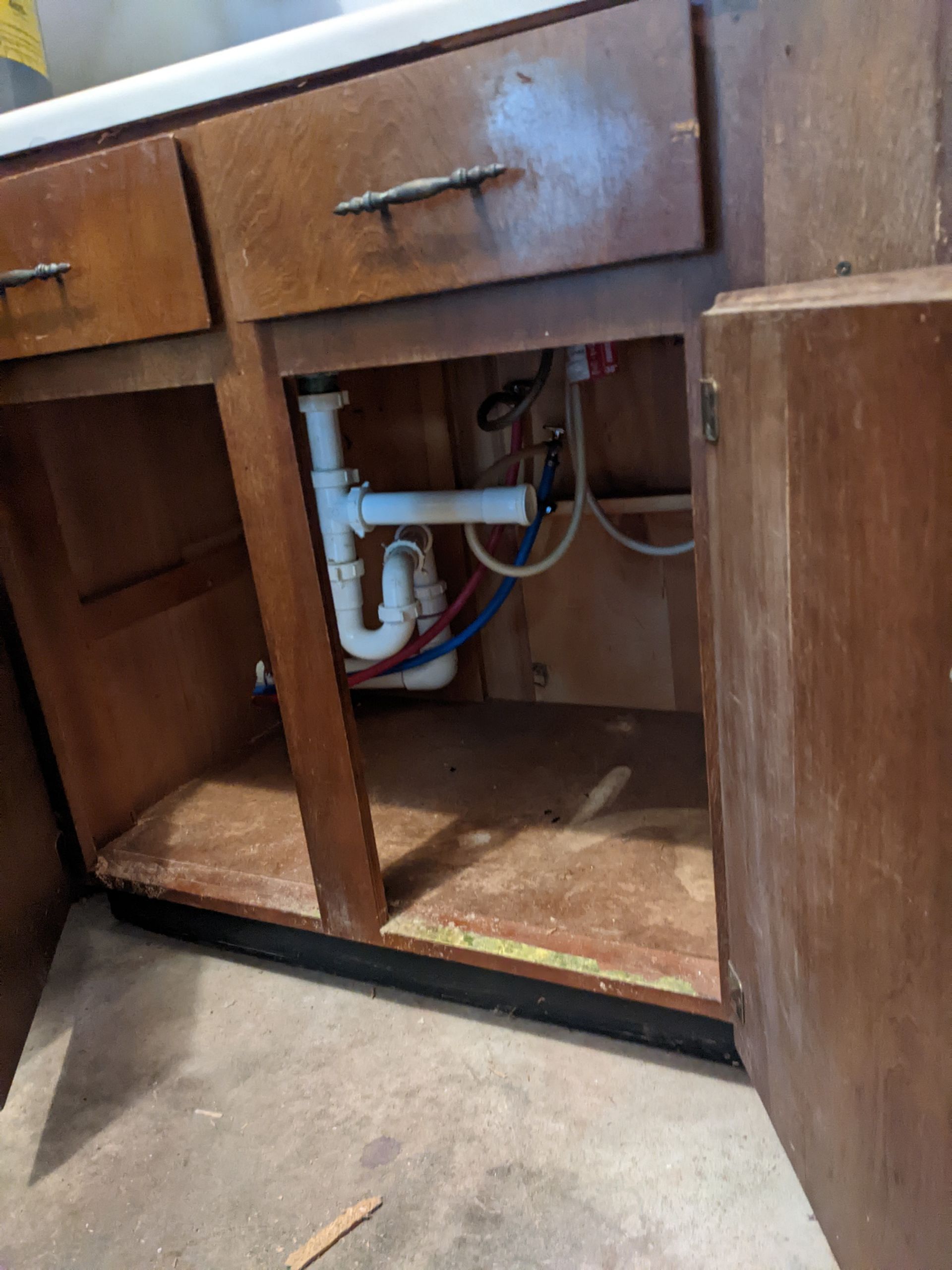A kitchen sink is under a wooden cabinet with the door open.