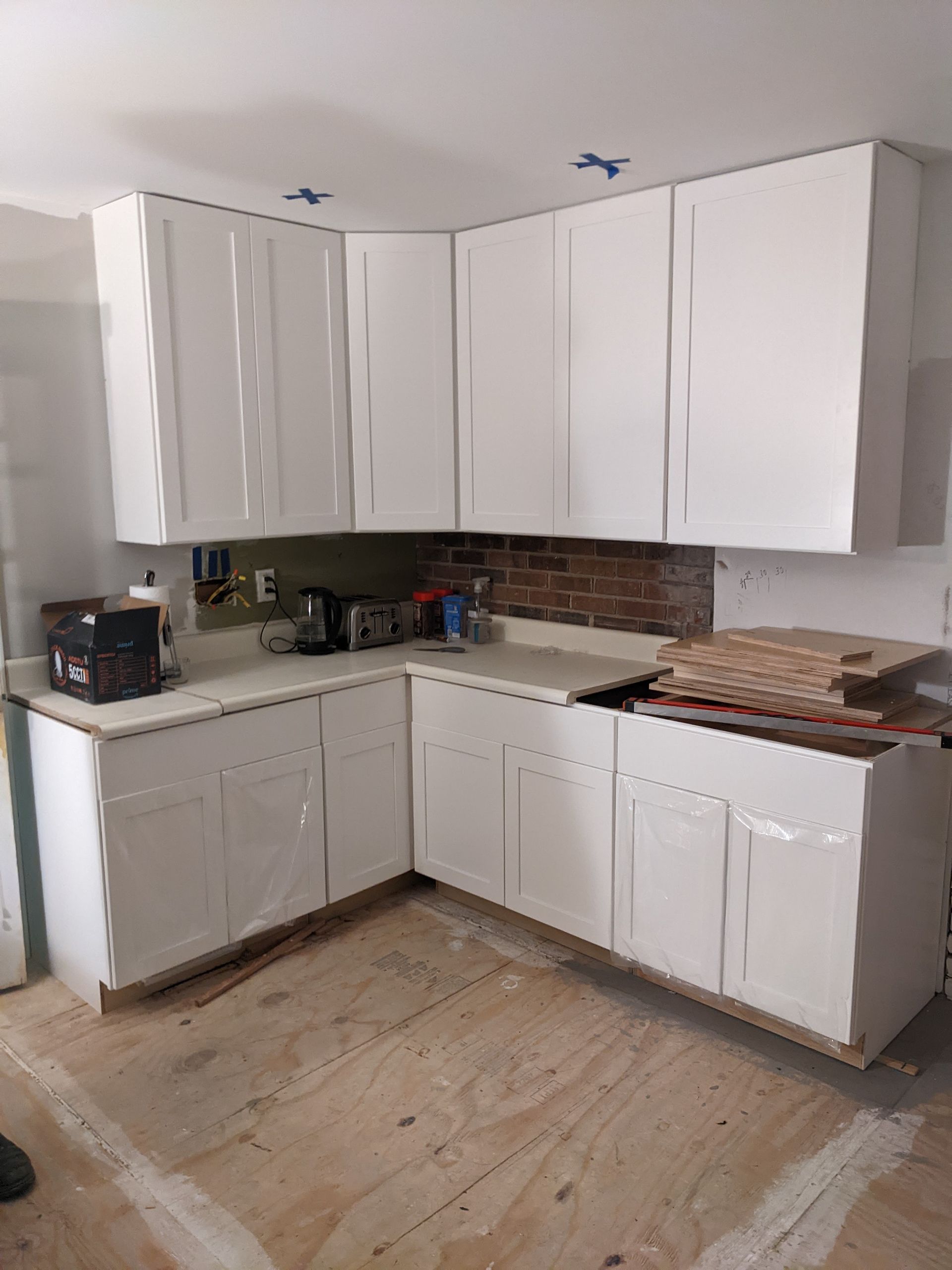 A kitchen under construction with white cabinets and a wooden floor.