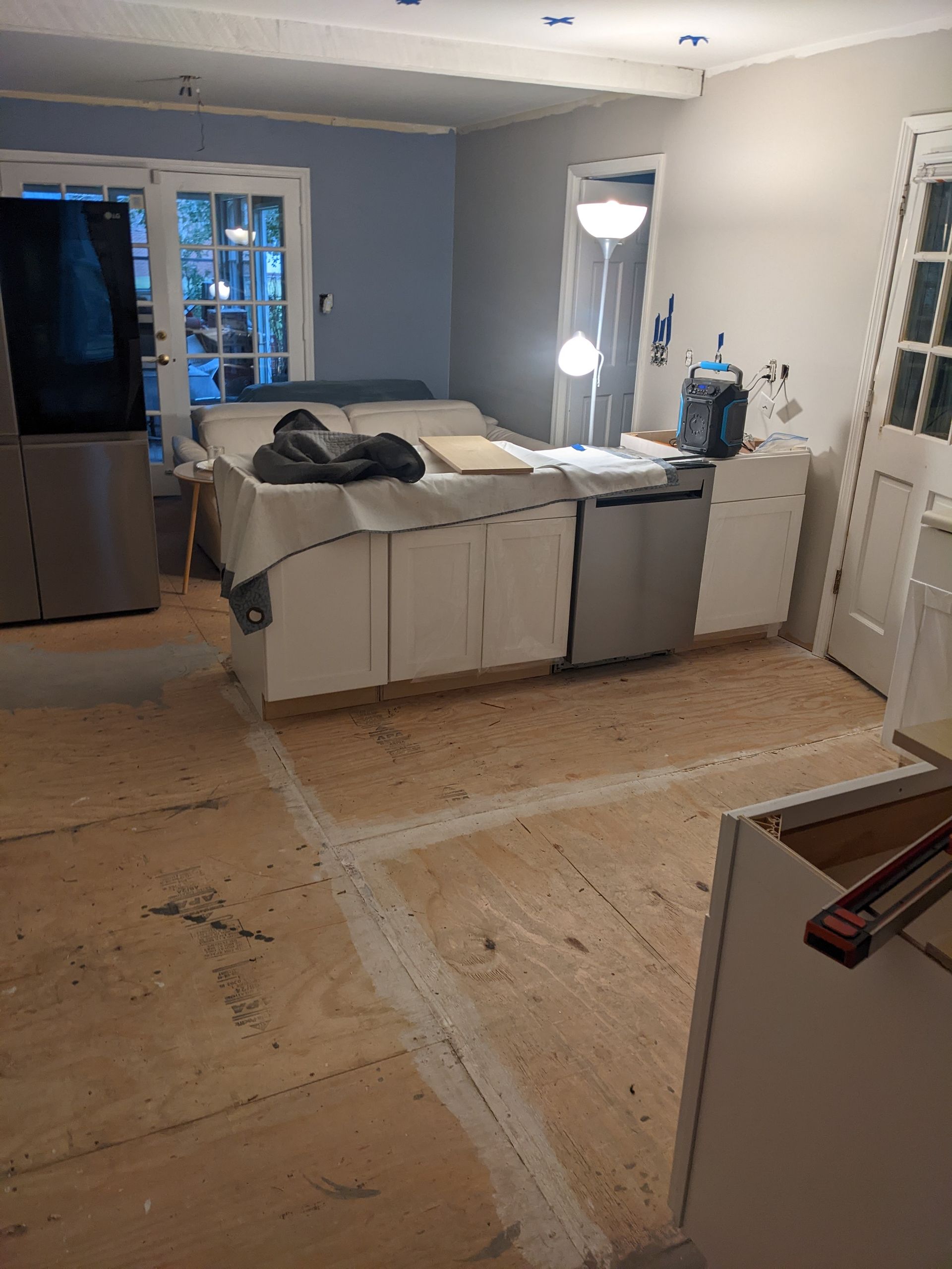 A kitchen under construction with a stainless steel refrigerator and dishwasher.