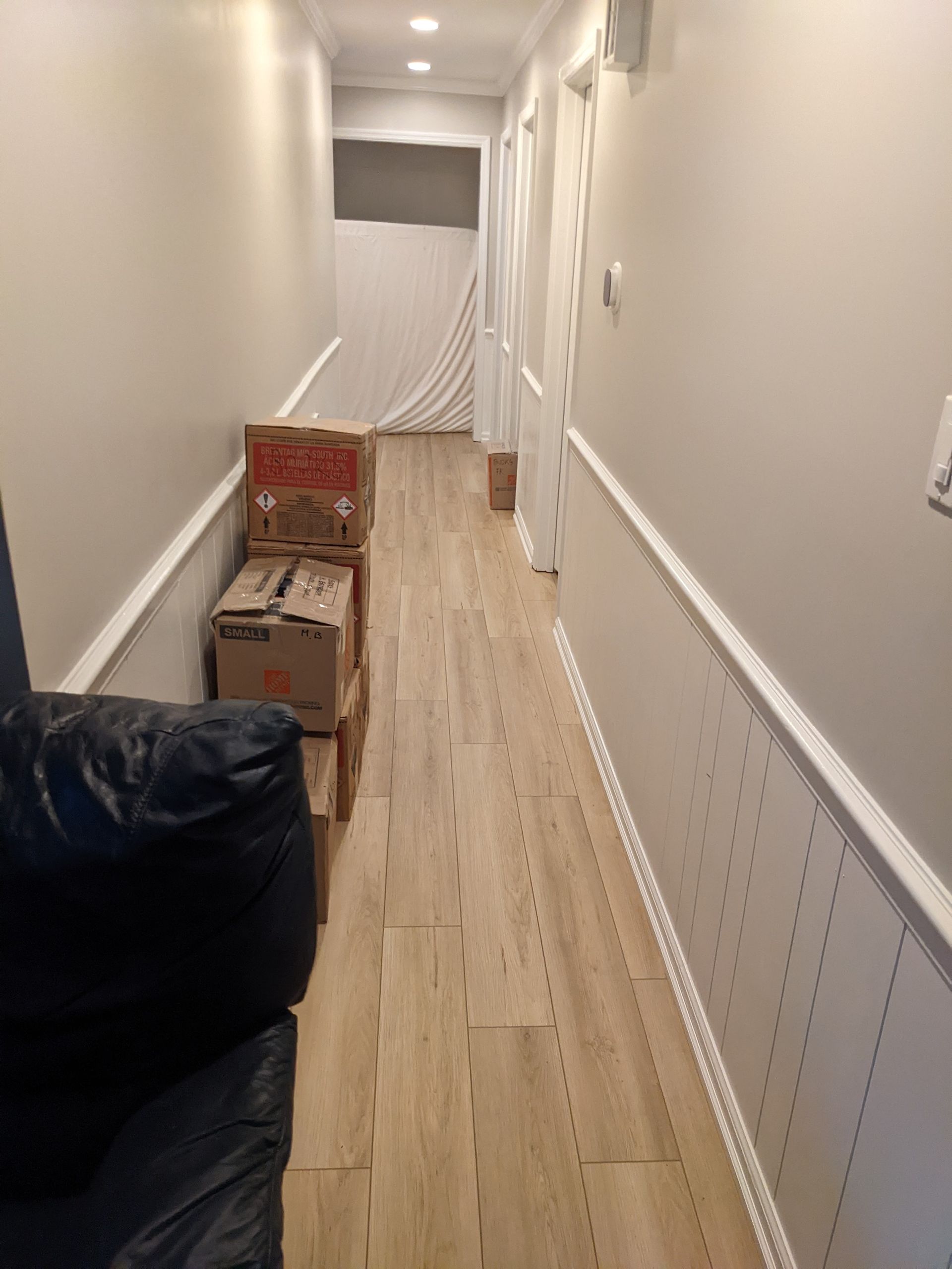 A long hallway with wooden floors and boxes on the floor.