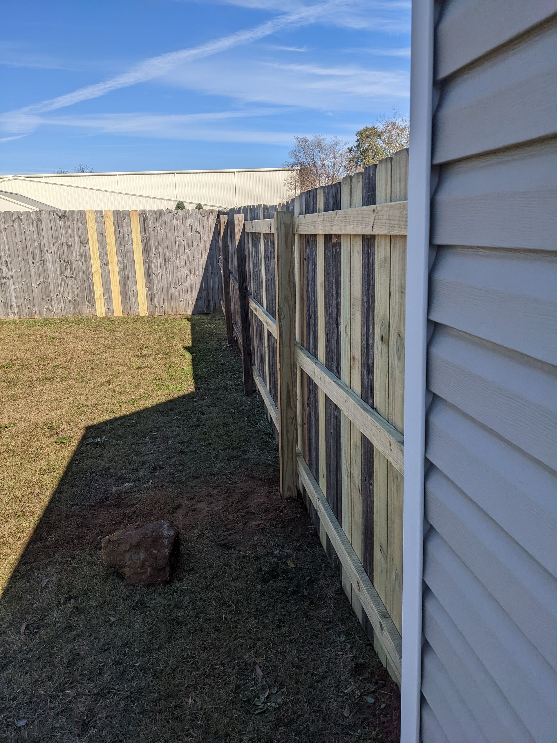 A wooden fence is next to a house in a backyard.
