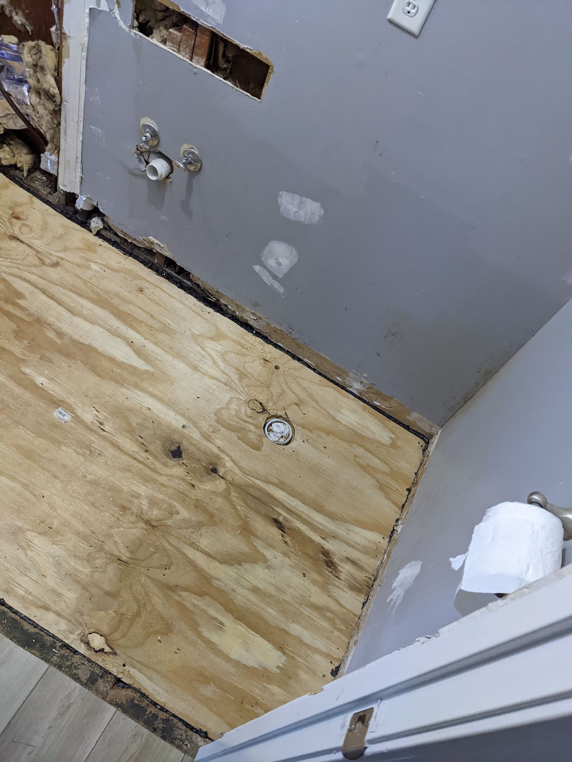 A bathroom with a hole in the wall and a wooden floor.