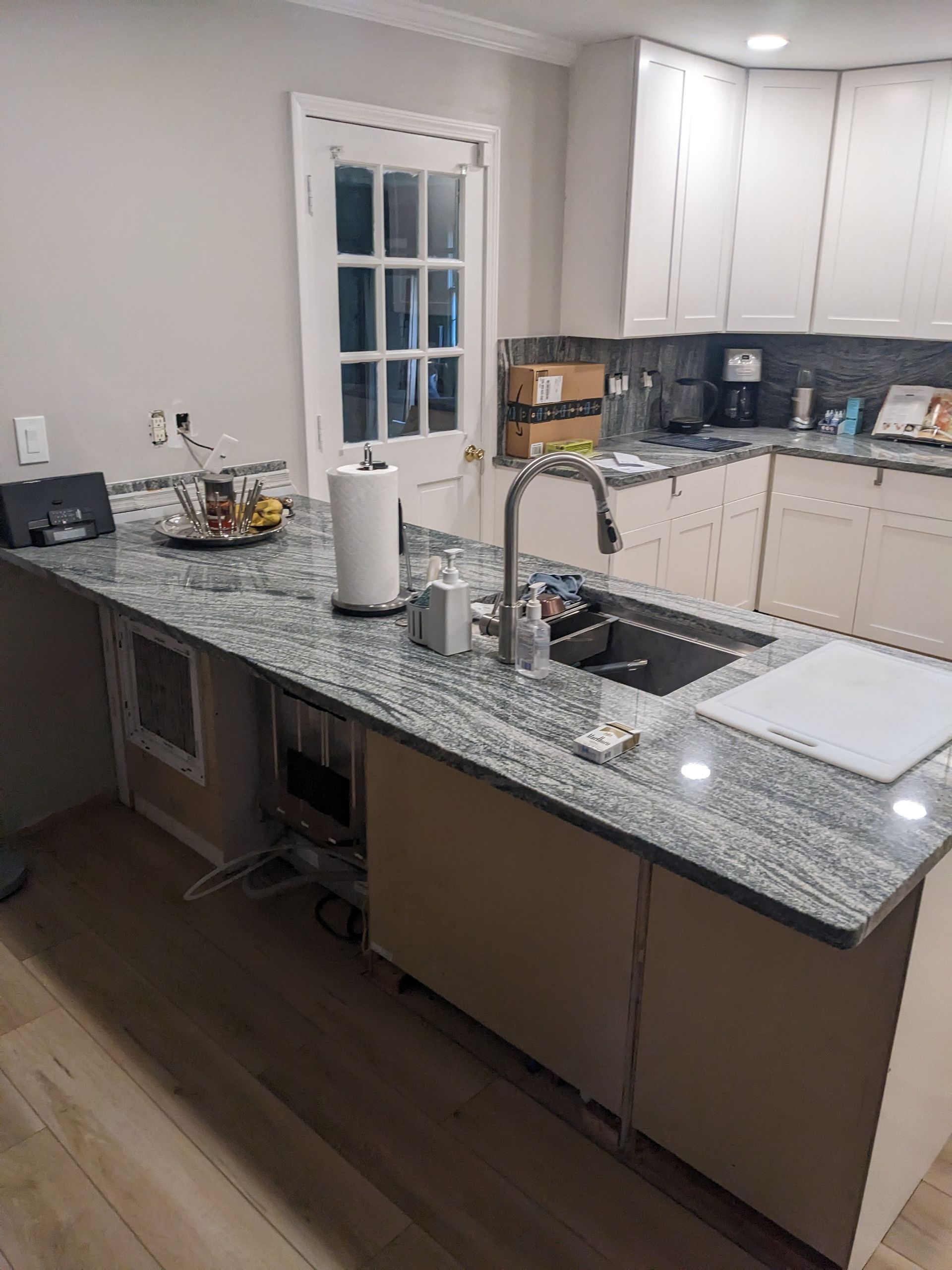 A kitchen with granite counter tops , white cabinets and a sink.