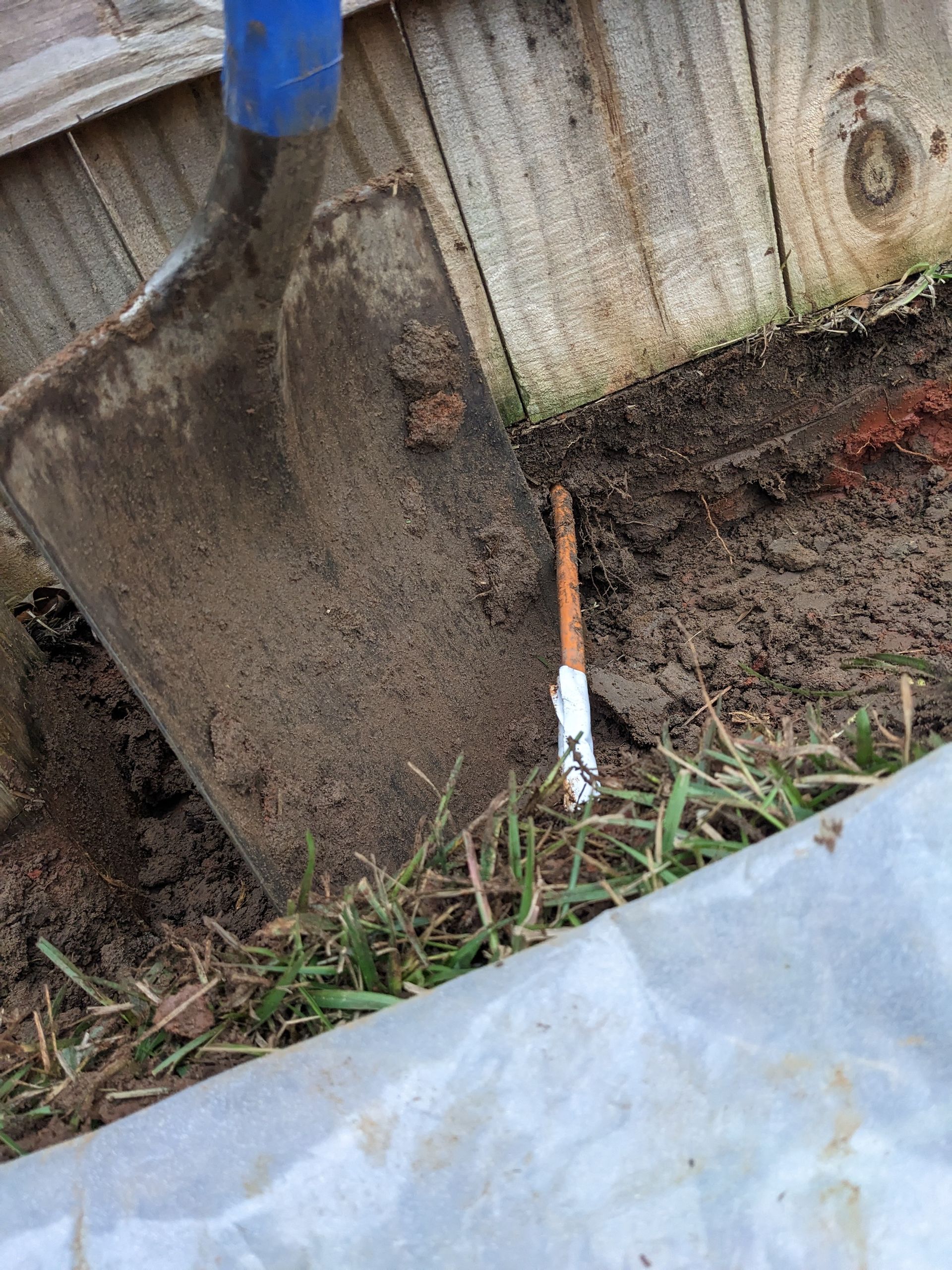 A shovel is sitting in the dirt next to a wooden fence.