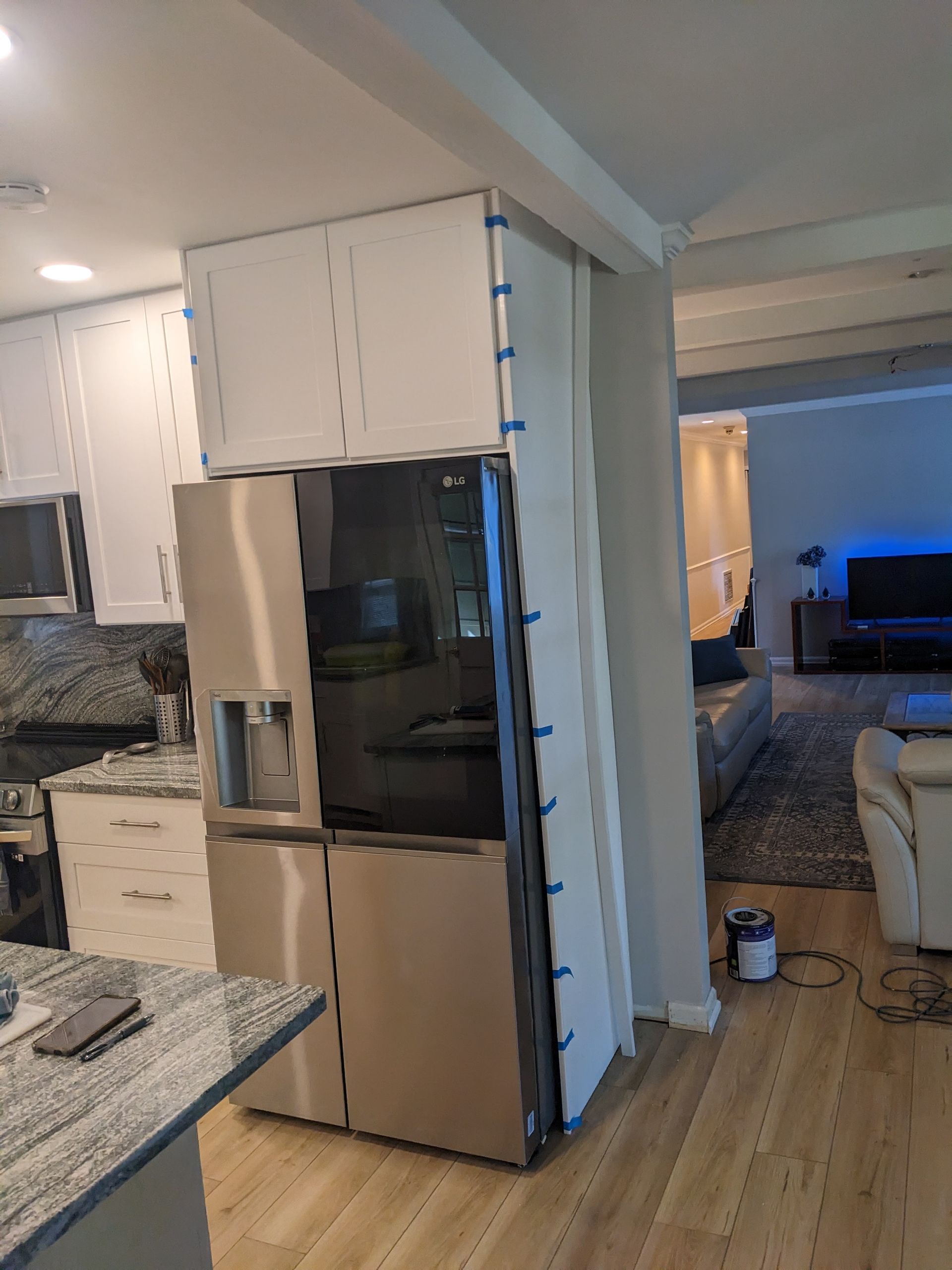 A stainless steel refrigerator is sitting in a kitchen next to a living room.
