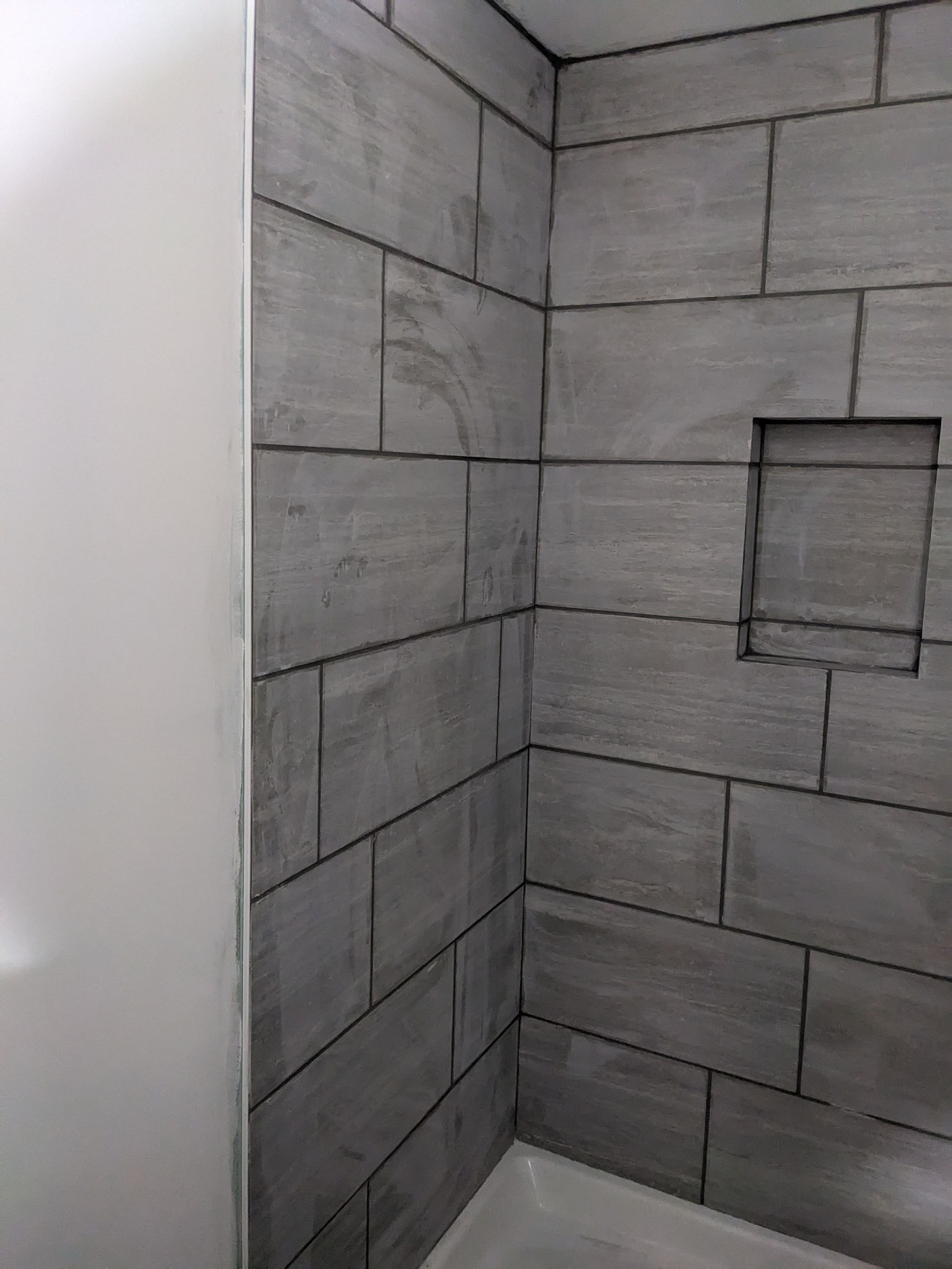 A bathroom with gray tile walls and a bathtub.