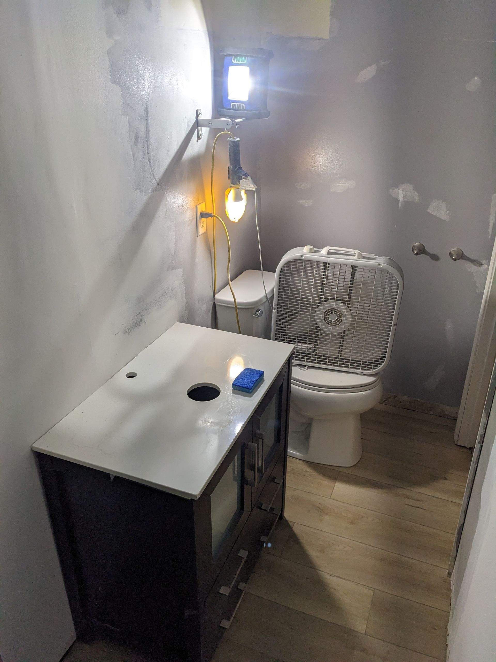 A bathroom with a toilet , sink , and fan.