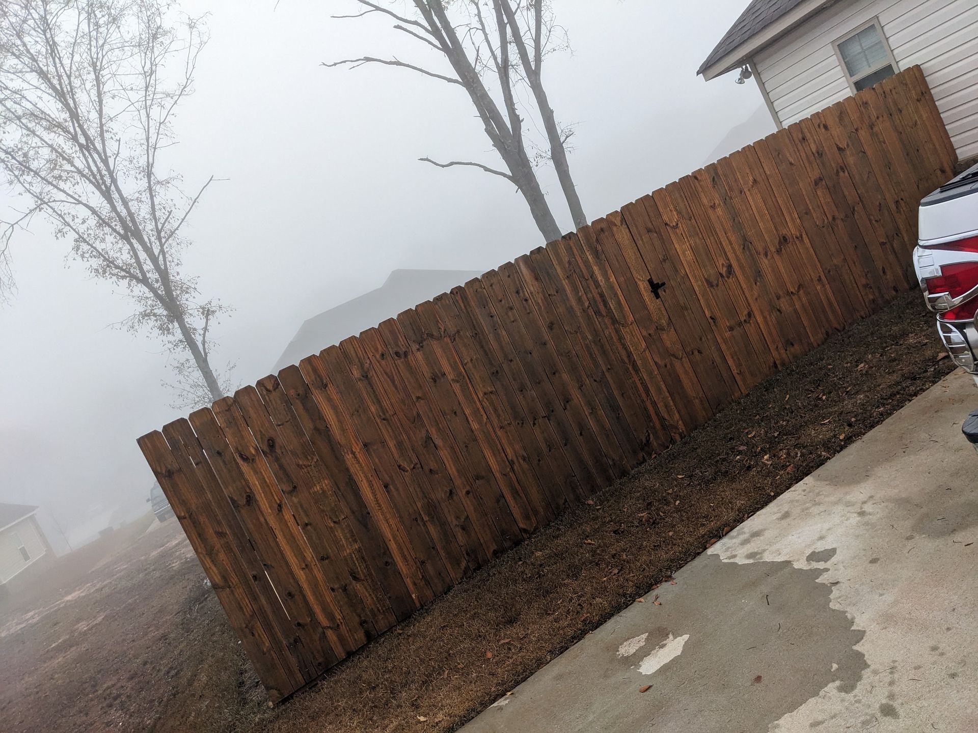 A wooden fence is surrounded by fog in front of a house.