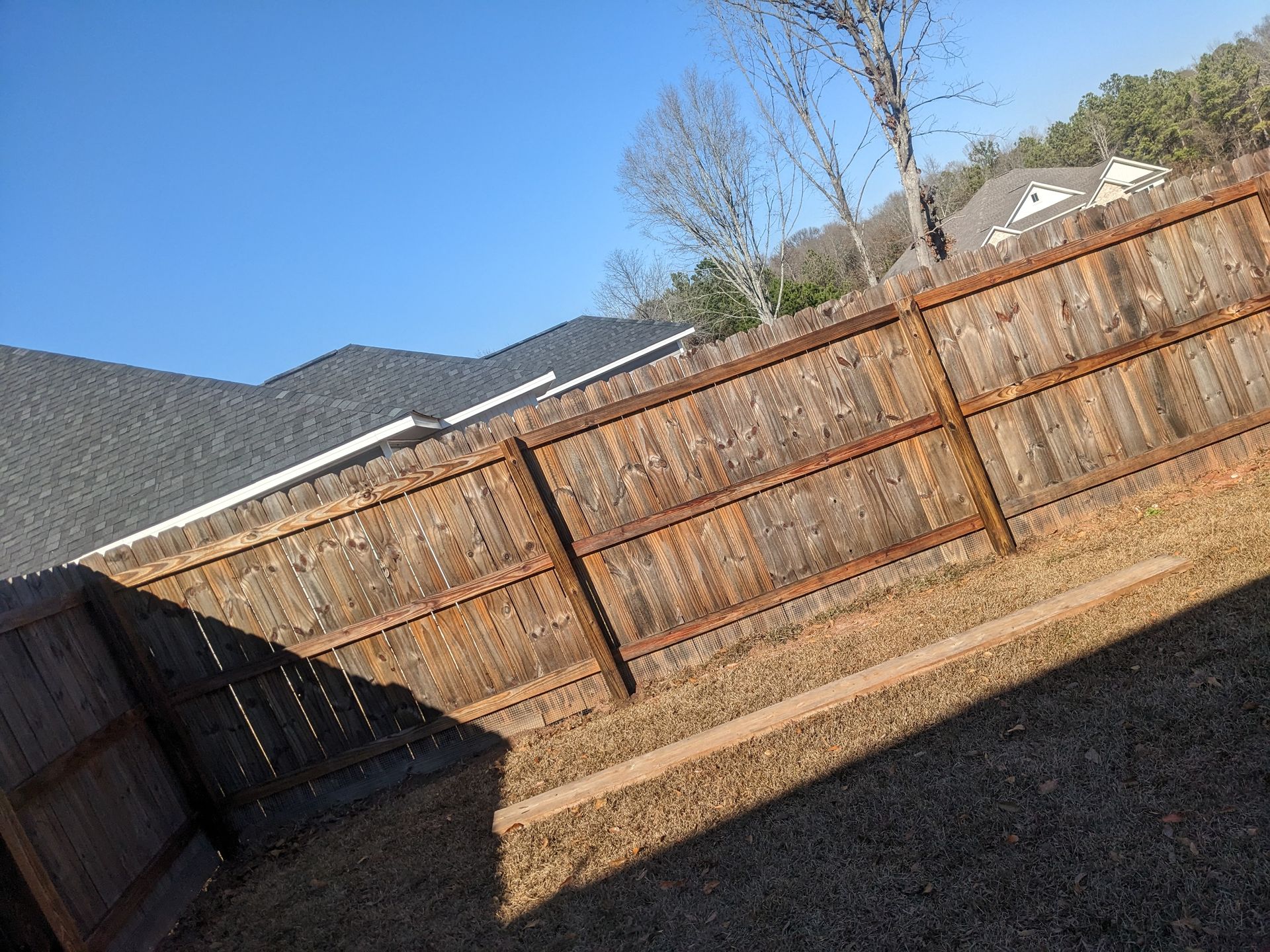 A wooden fence in a backyard with a house in the background.