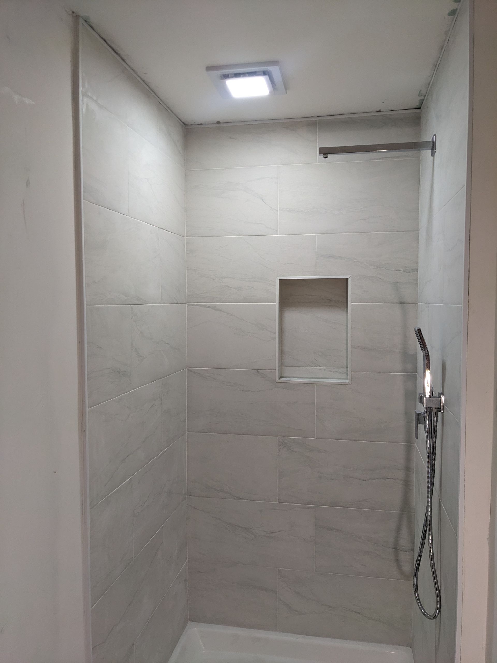 A shower with a shower head and a light on the ceiling.