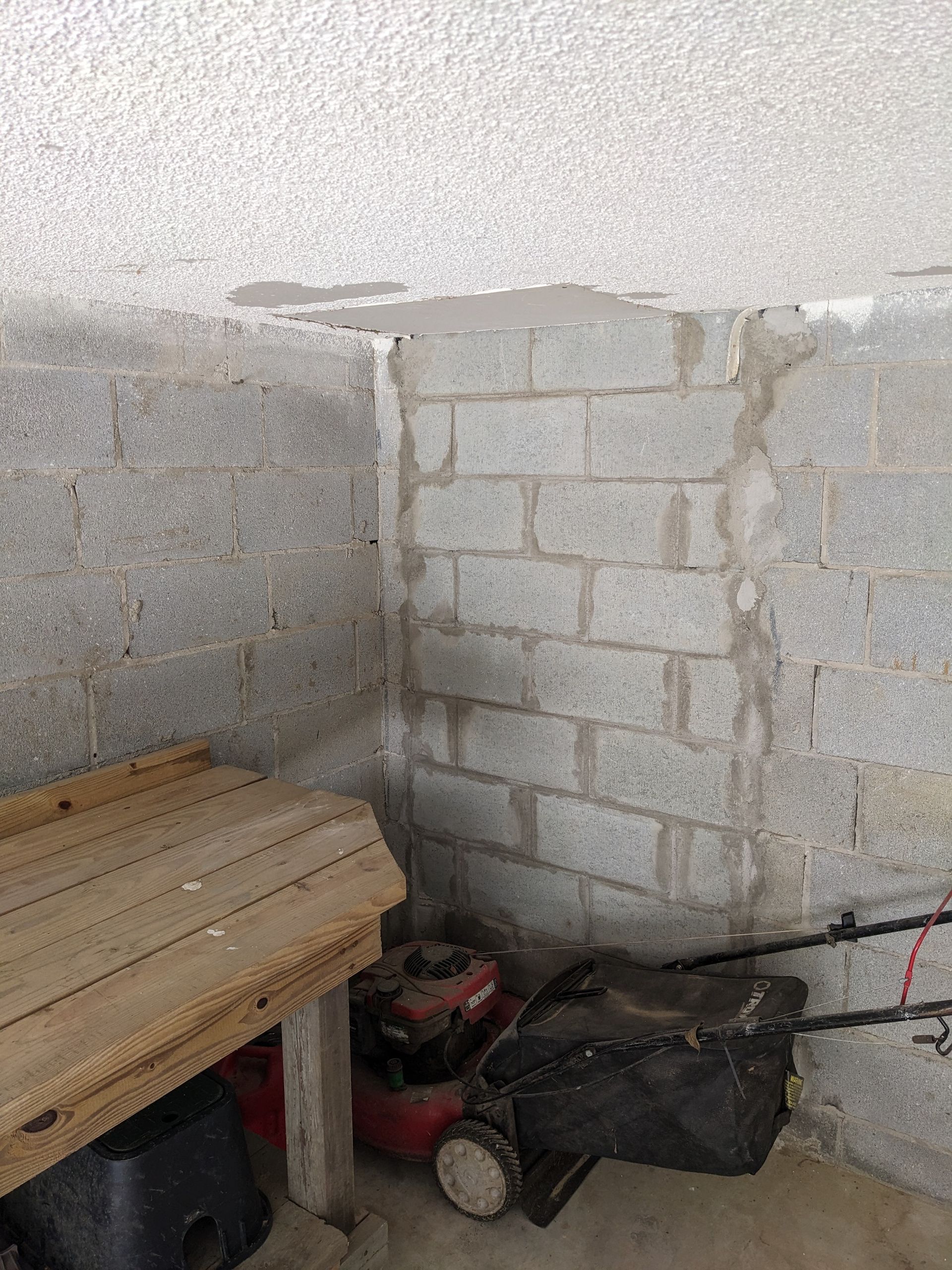 A lawn mower is parked in a corner of a room next to a wooden bench.