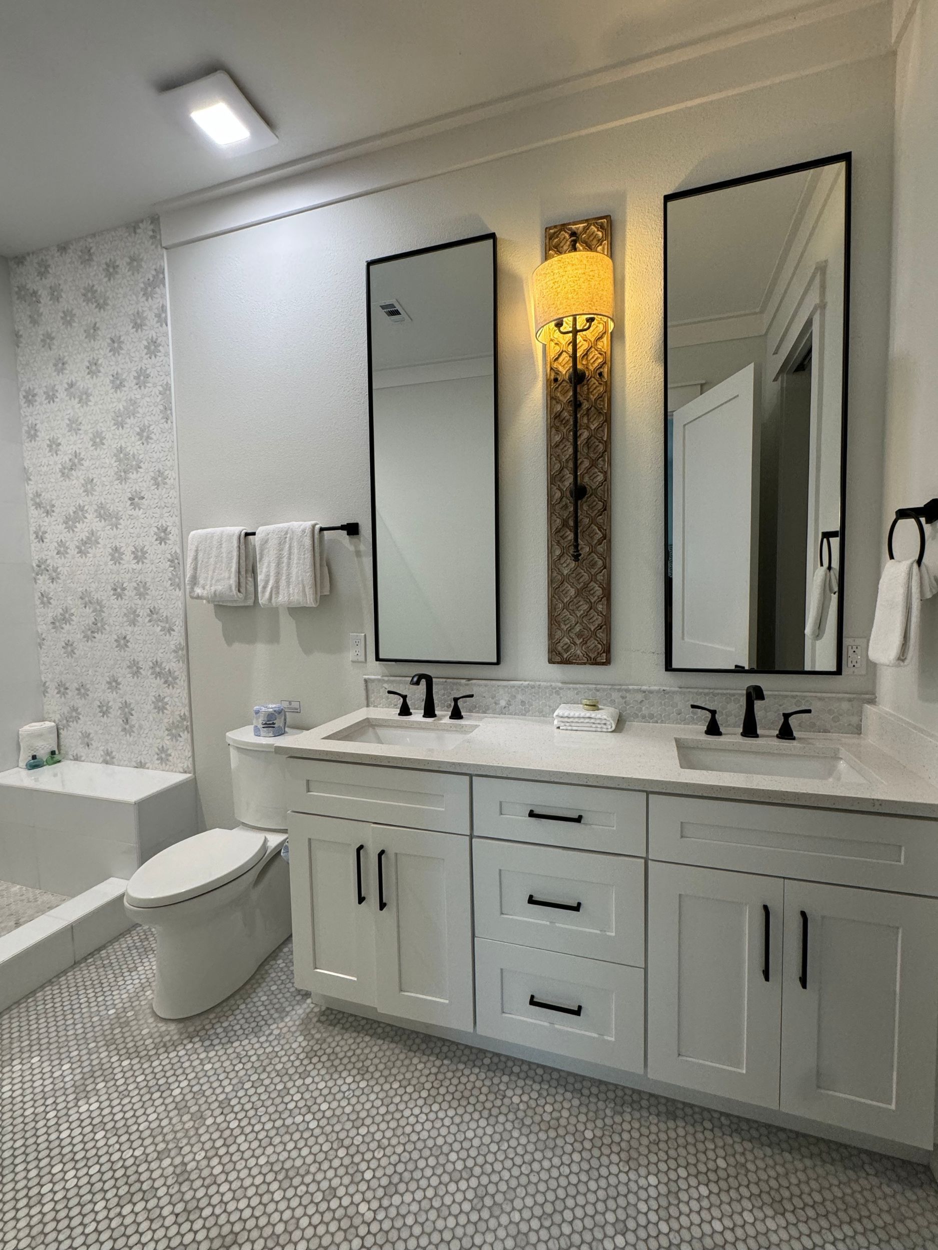 A bathroom with two sinks , a toilet , and two mirrors.