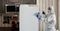 A man in a protective suit is cleaning a refrigerator in a kitchen.