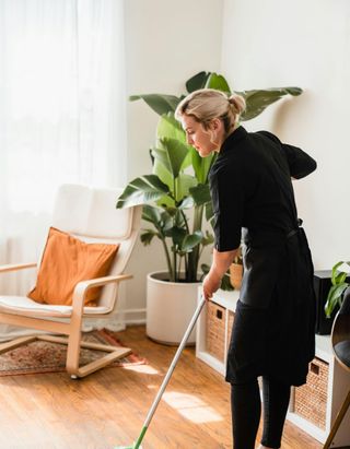 A woman is cleaning the floor of a living room with a mop.