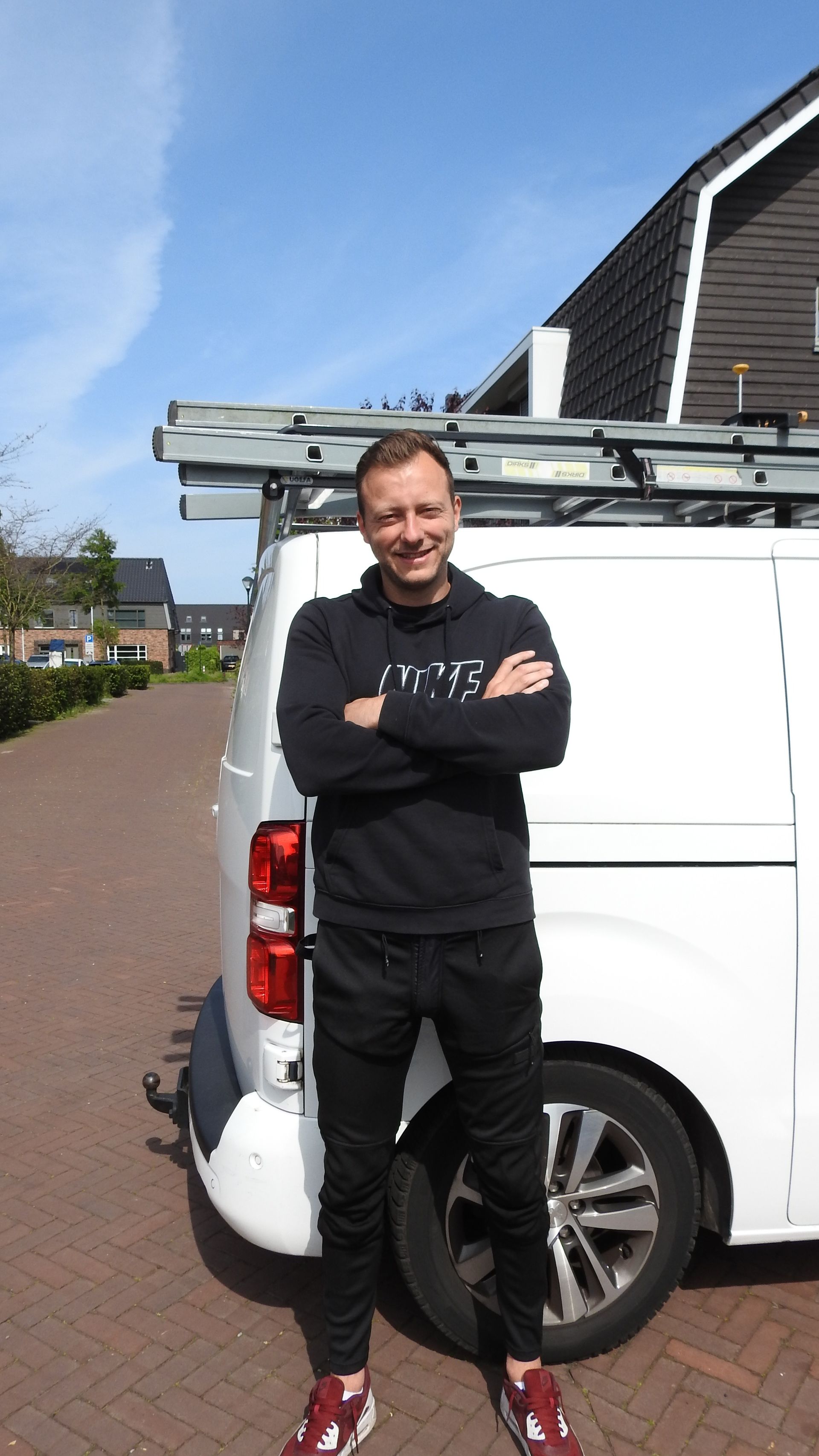 Een man staat met zijn armen over elkaar voor een wit busje.