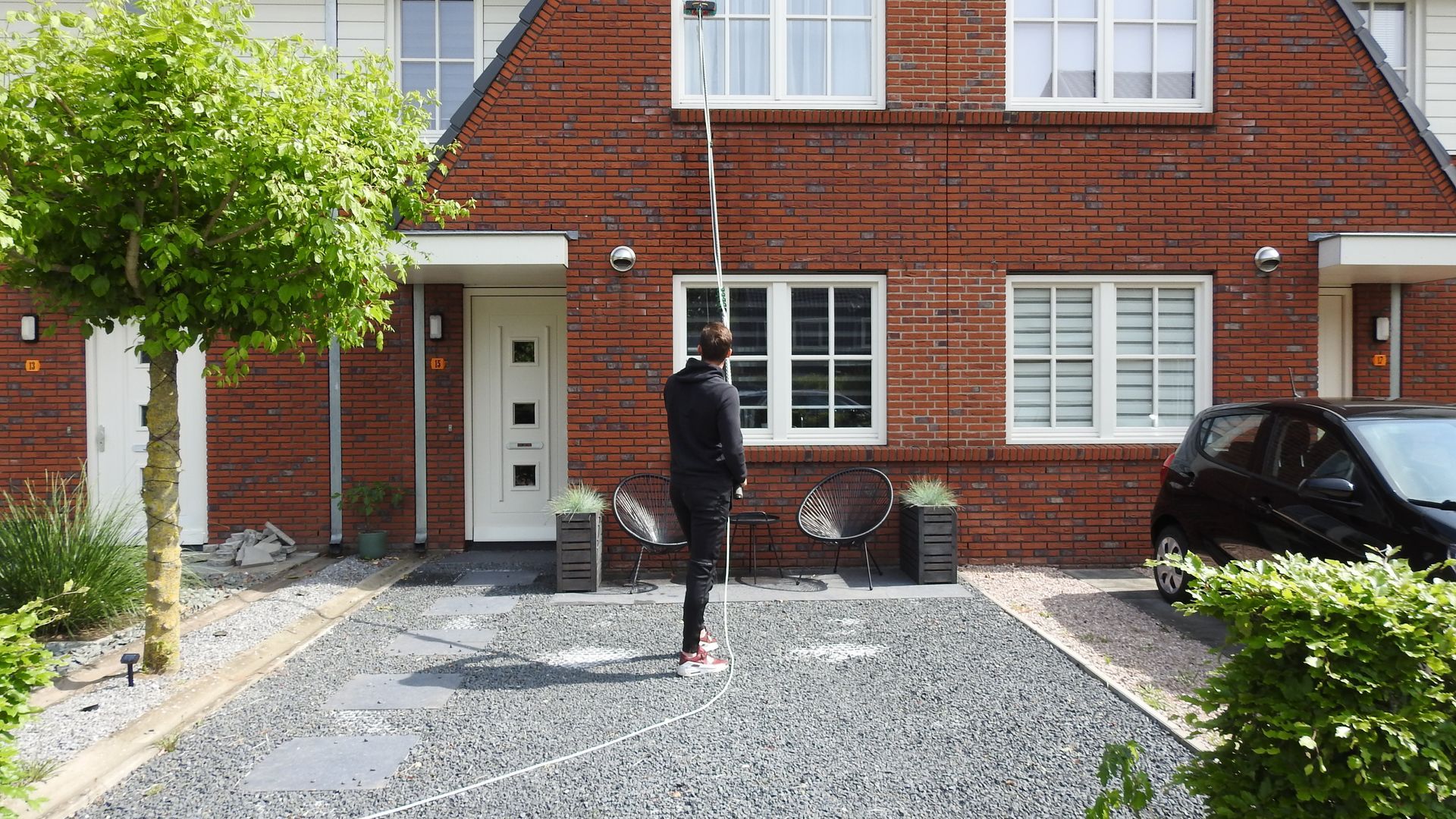 Voor een bakstenen huis staat een man met een auto ervoor geparkeerd.