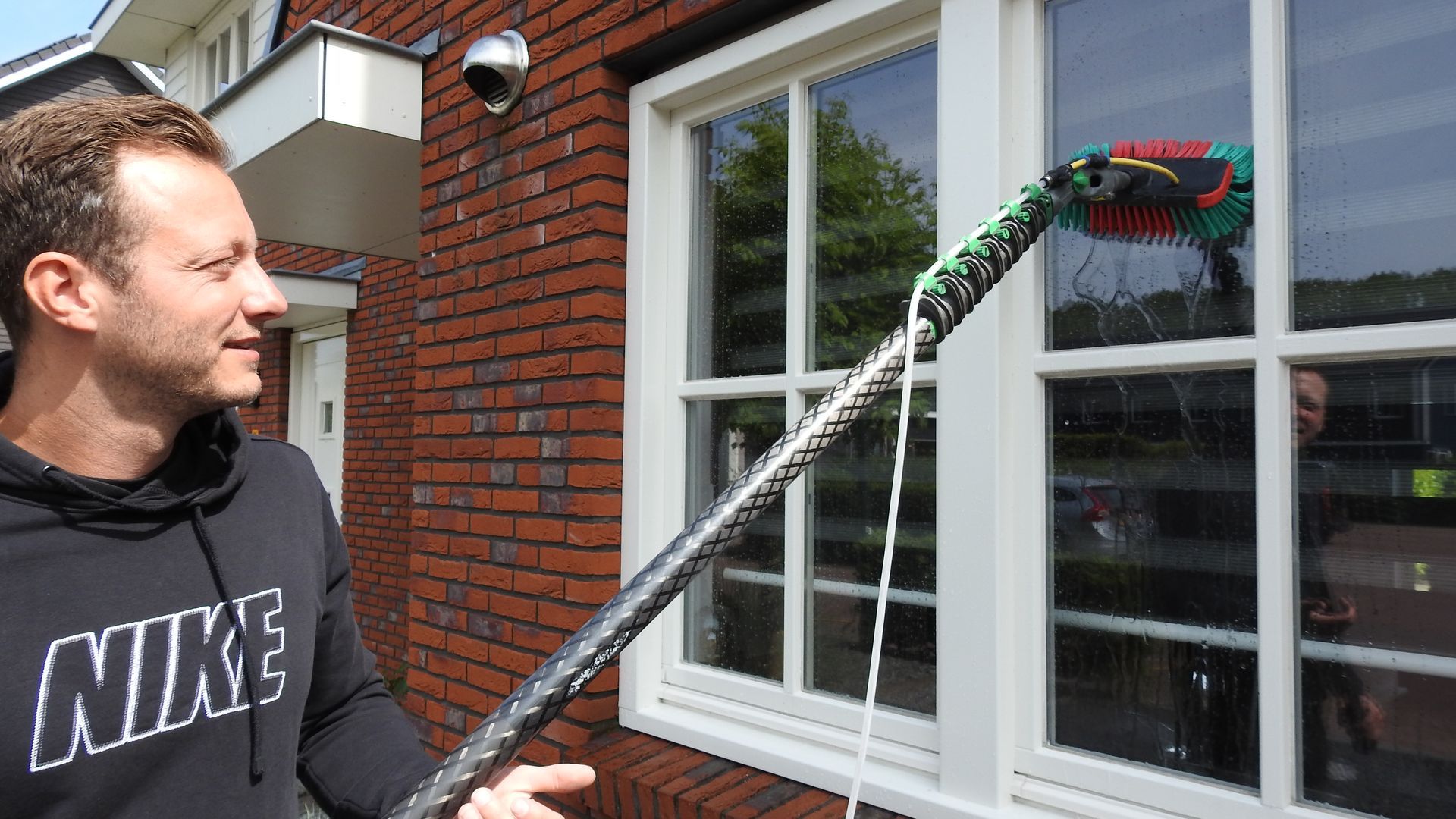 Een man maakt een raam schoon met een lange steel.