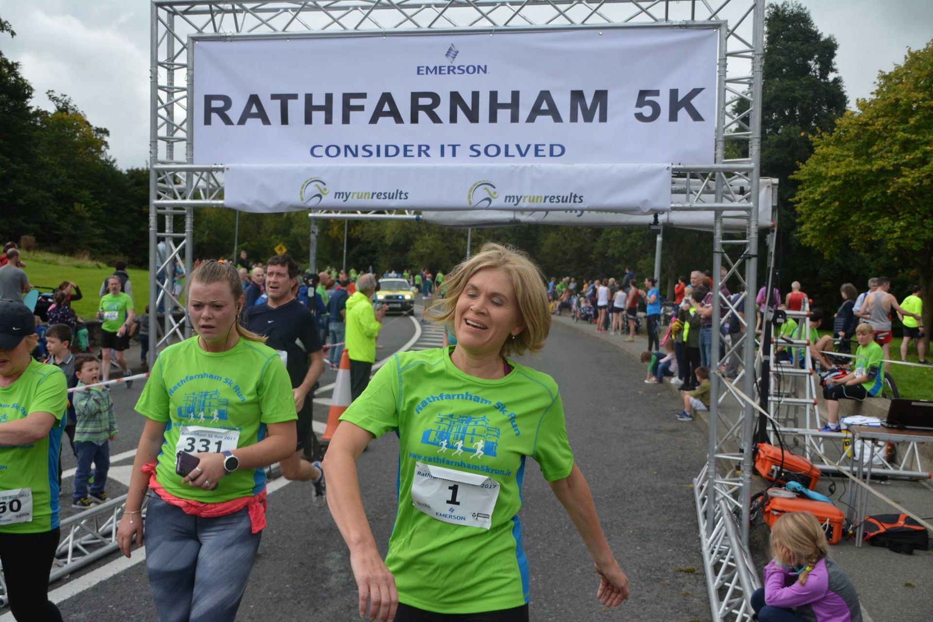 A woman in a green shirt is standing in front of a sign that says rathfarnham 5k