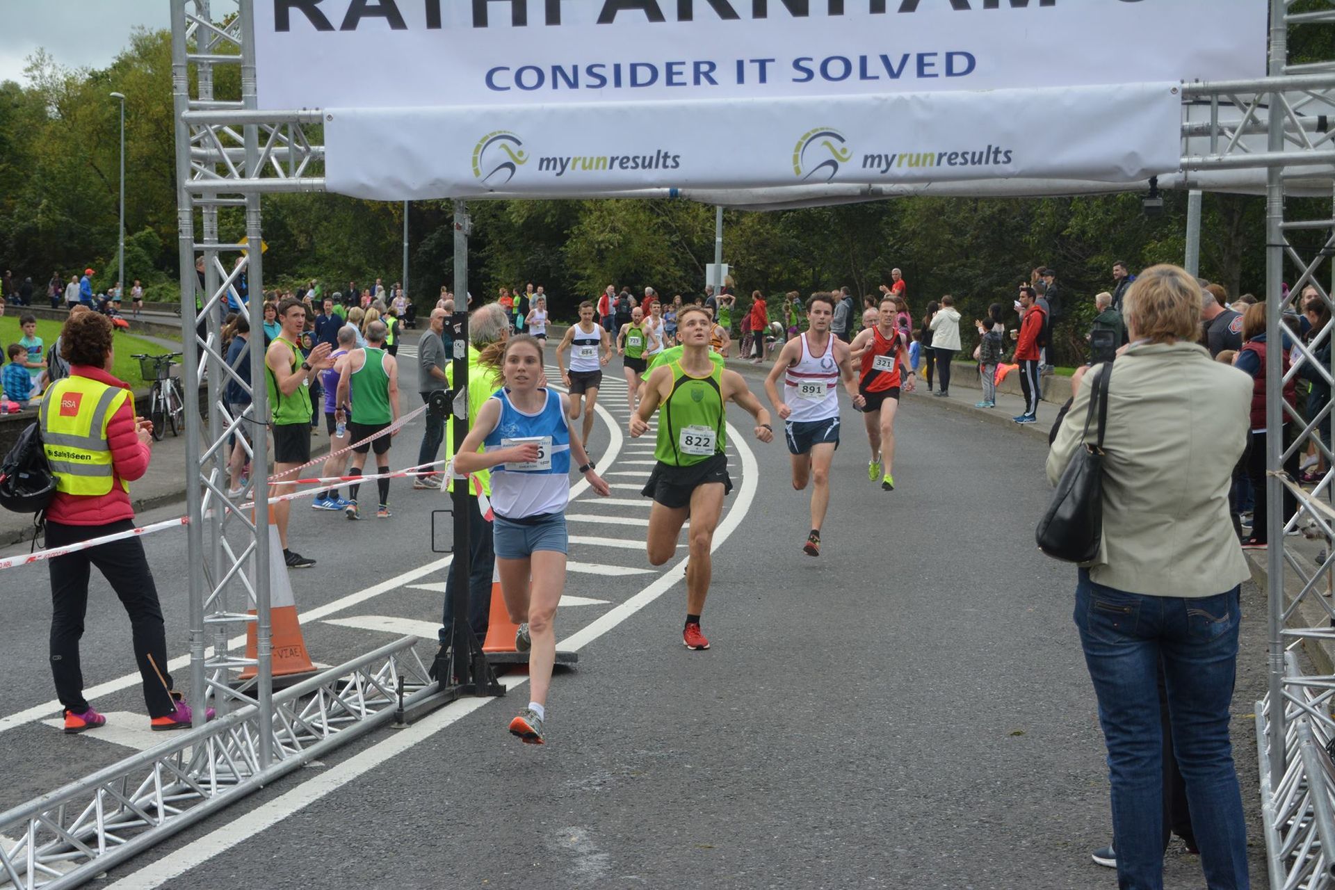 A woman taking a picture of a group of runners in front of a banner that says 