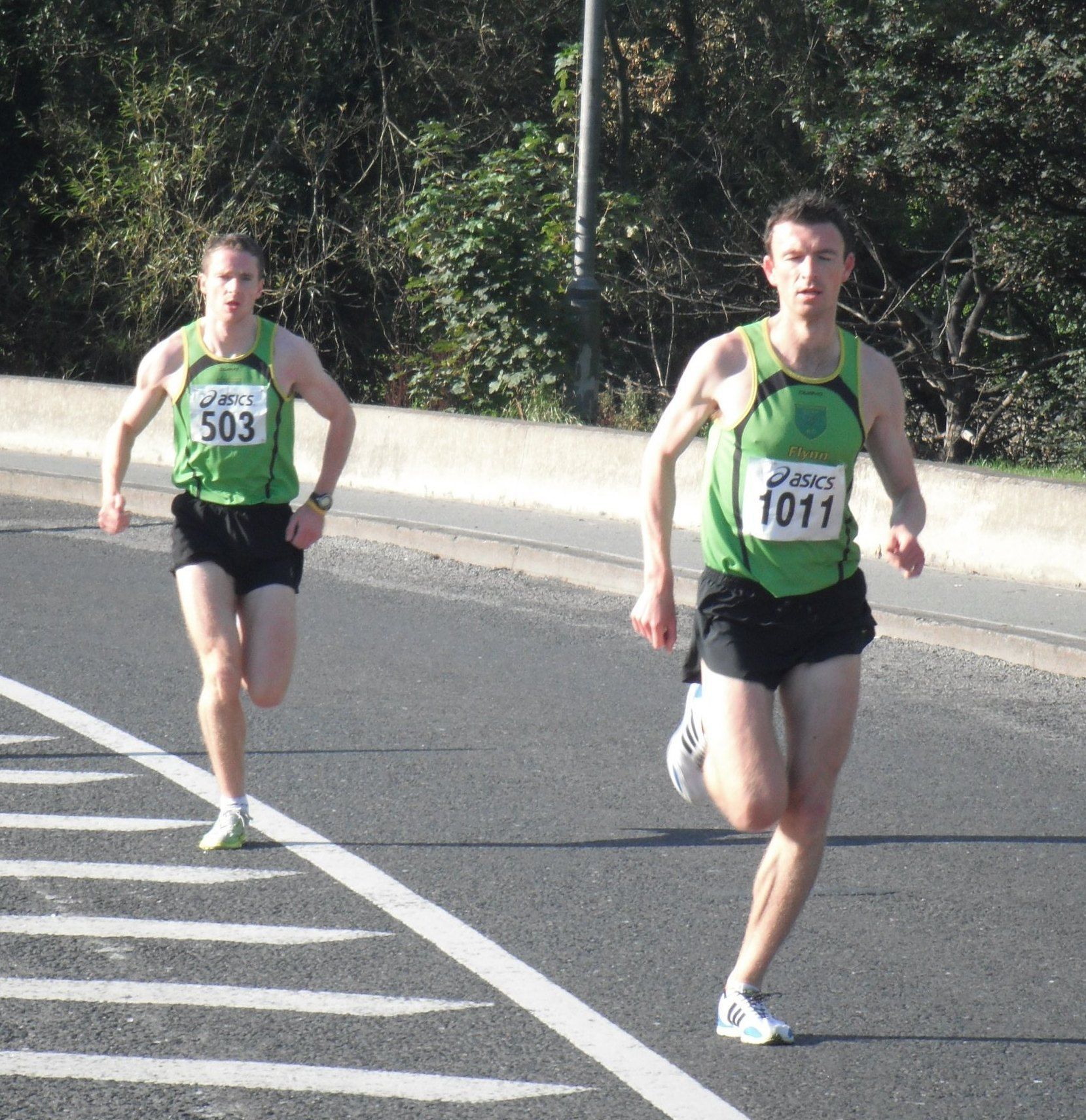Two men are running on a road and one has the number 1011 on his shirt