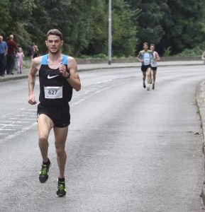 A man wearing a nike tank top and shorts is running down a road.