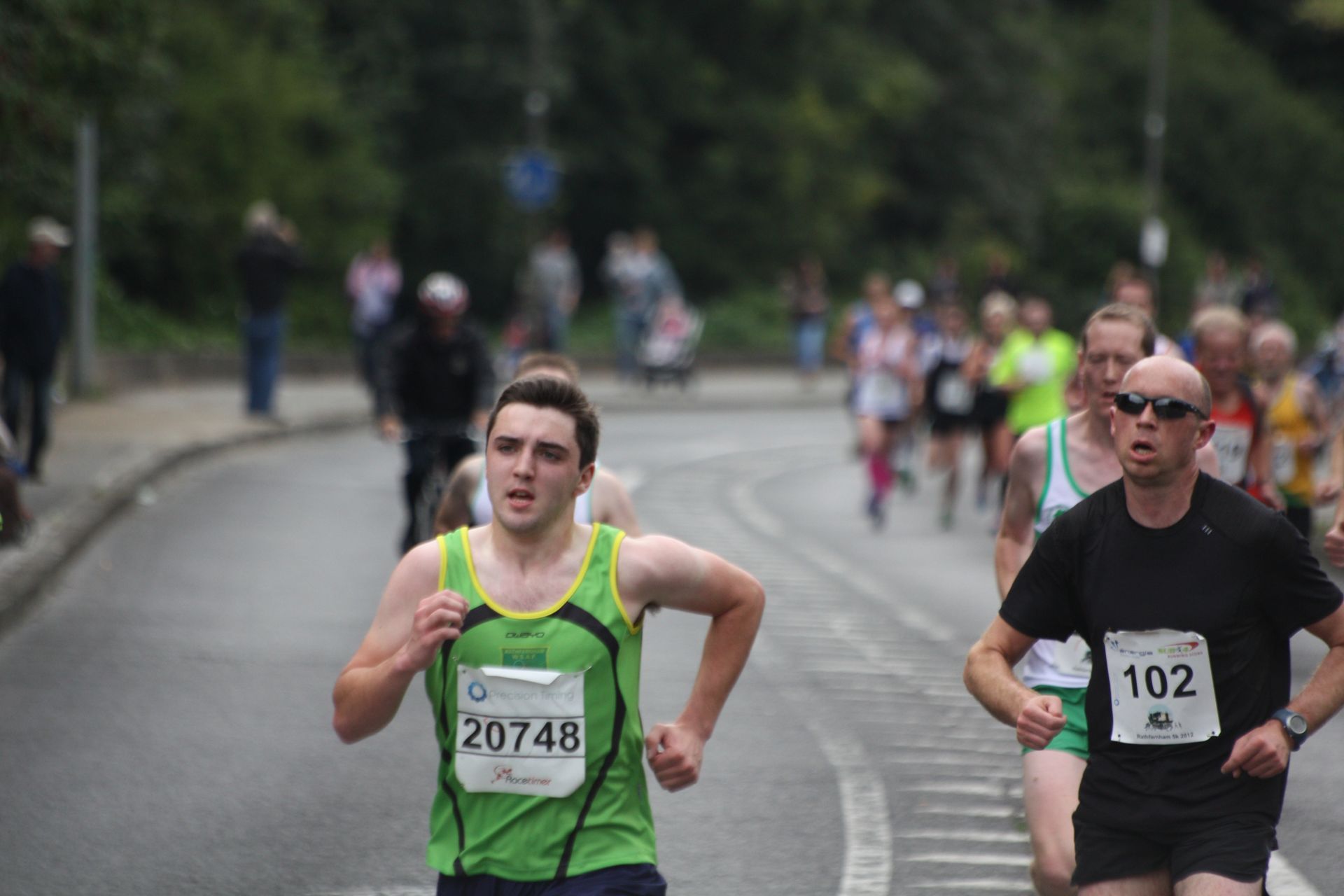 A man in a green tank top is running in a marathon.