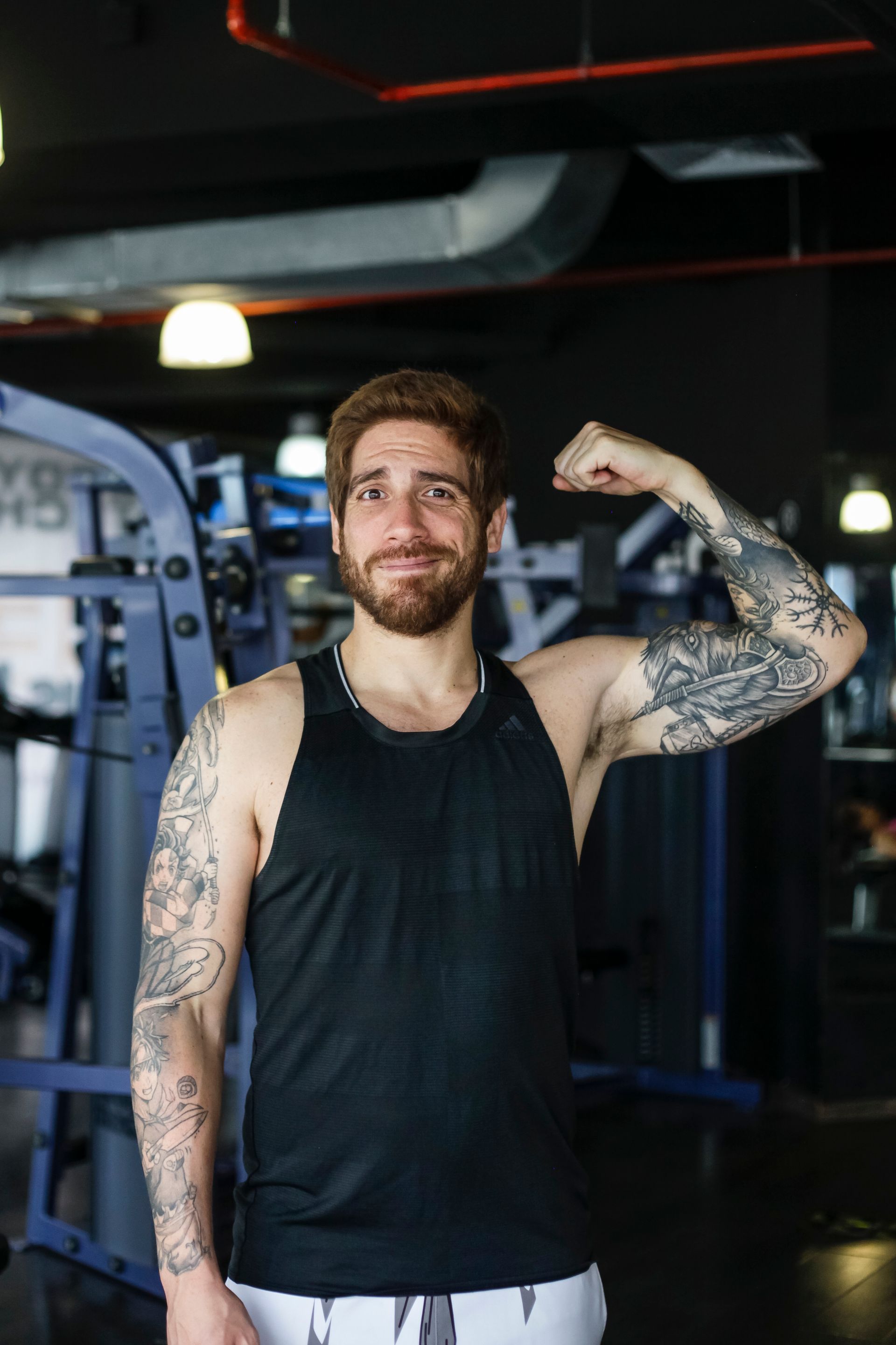 Un hombre con barba y tatuajes está flexionando sus músculos en un gimnasio.