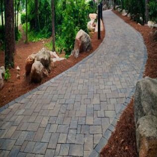 A brick path winds through a forest, bordered by rocks and mulch.