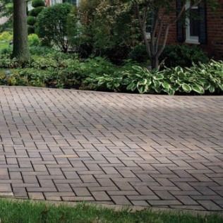 Brick paver driveway in front of a house, surrounded by greenery.
