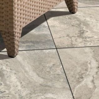 Close-up of a woven chair leg on light-colored stone patio tiles with dark grout lines.