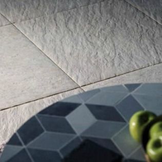 Textured light gray tile floor, partially framed by a dark blue and gray geometric table with green apples.