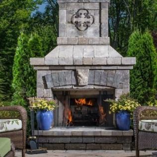 Outdoor stone fireplace with burning fire and potted yellow flowers.