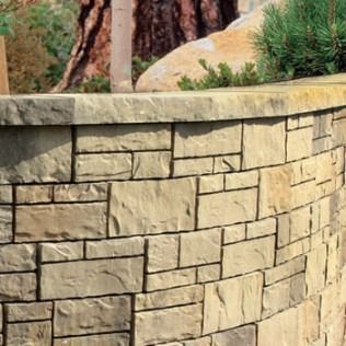 Curved stone retaining wall with various rectangular blocks, in shades of tan and brown.