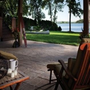 Wooden porch overlooking a lake, with canoe, chairs, and mug.