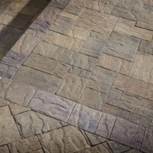 Textured stone patio with rectangular and square blocks in shades of brown and gray.