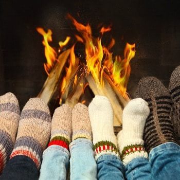 Feet in colorful socks warming by a fireplace.