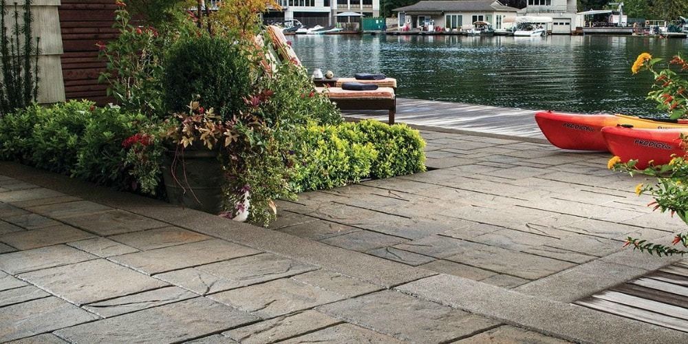 Patio near a lake with plants, a red kayak, and buildings in the background.