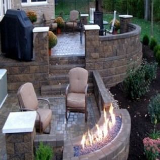 Patio with stone walls, steps, and a fire pit; seating, grill, and landscaping visible.