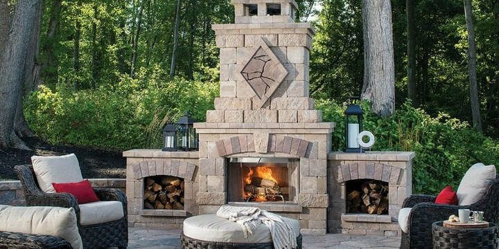 Outdoor fireplace with seating. Fire is lit. Stone structure and forest background.