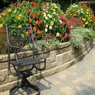 Black chair on a stone patio, with a raised garden bed filled with colorful flowers.