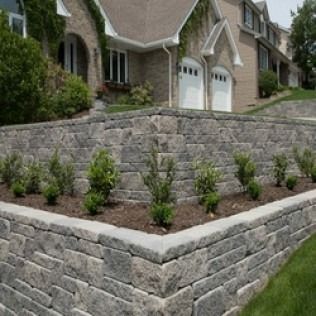 Stone retaining walls with tiered planters in front of a multi-story brick house.