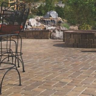 Brick patio with a waterfall, fire pit, and metal chair.