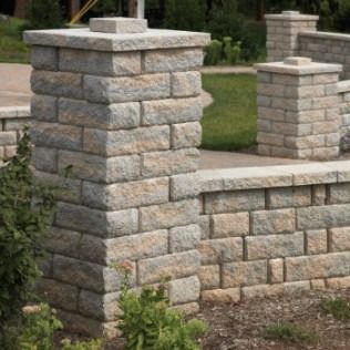 Stone pillars and wall in a landscaped setting; beige and gray colors.