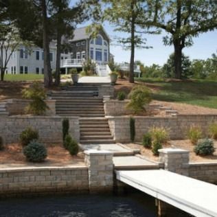 Stone steps and retaining walls lead up to a large house with a dock on the water.