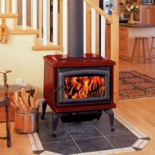 Red wood-burning stove with flames, chimney, on a tiled hearth, near stairs, and wooden floor.